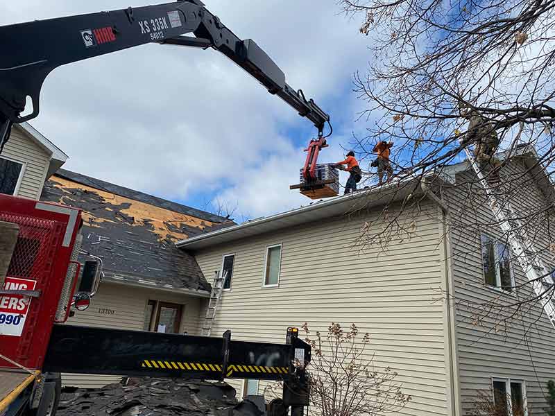 Clear Point Construction, Inc. workers on a roof grabbing packs of shingles from a crane delivering it to them