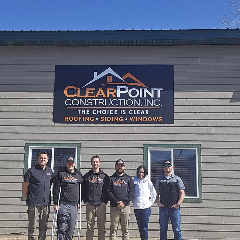 The Clear Point Construction, Inc. team in front of a home they are working on for Habitat for Humanity, holding a sign with their logo, services, website, and credentials on it